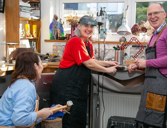 Man and Two Ladies Creating Jewellery in a Goldsmiths Workshop, Everyone is Smiling