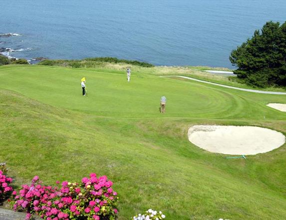 Photo of golfers in play on the green with waters of Belfast Lough in background