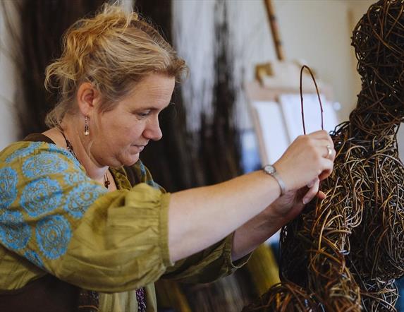 A lady at work on a weaving sculpture resembling a person