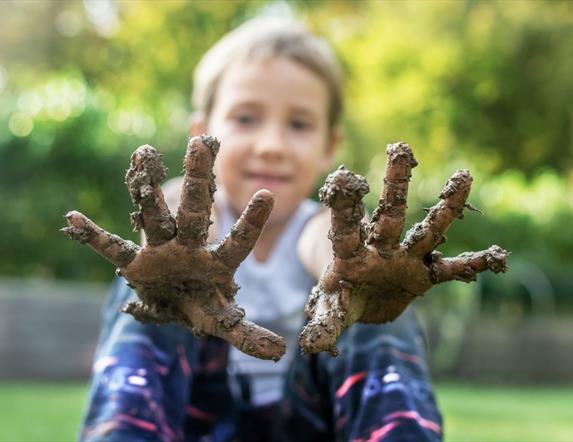 A child holding muddy hands up to the camera.