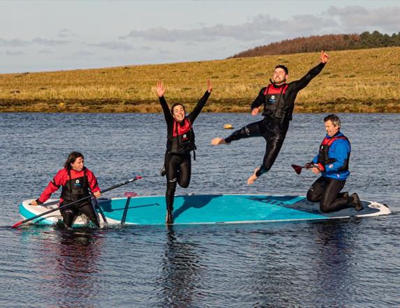 Four people jumping off a paddleboard into water