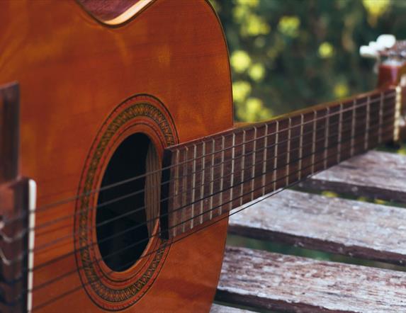 A close up of a guitar resting on a wooden table outdoors.
