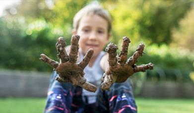 A child holding muddy hands up to the camera.