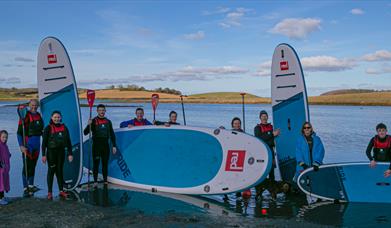 Paddleboarders of all ages standing with boards and paddles back from a session on the waters of Ballymoran Bay