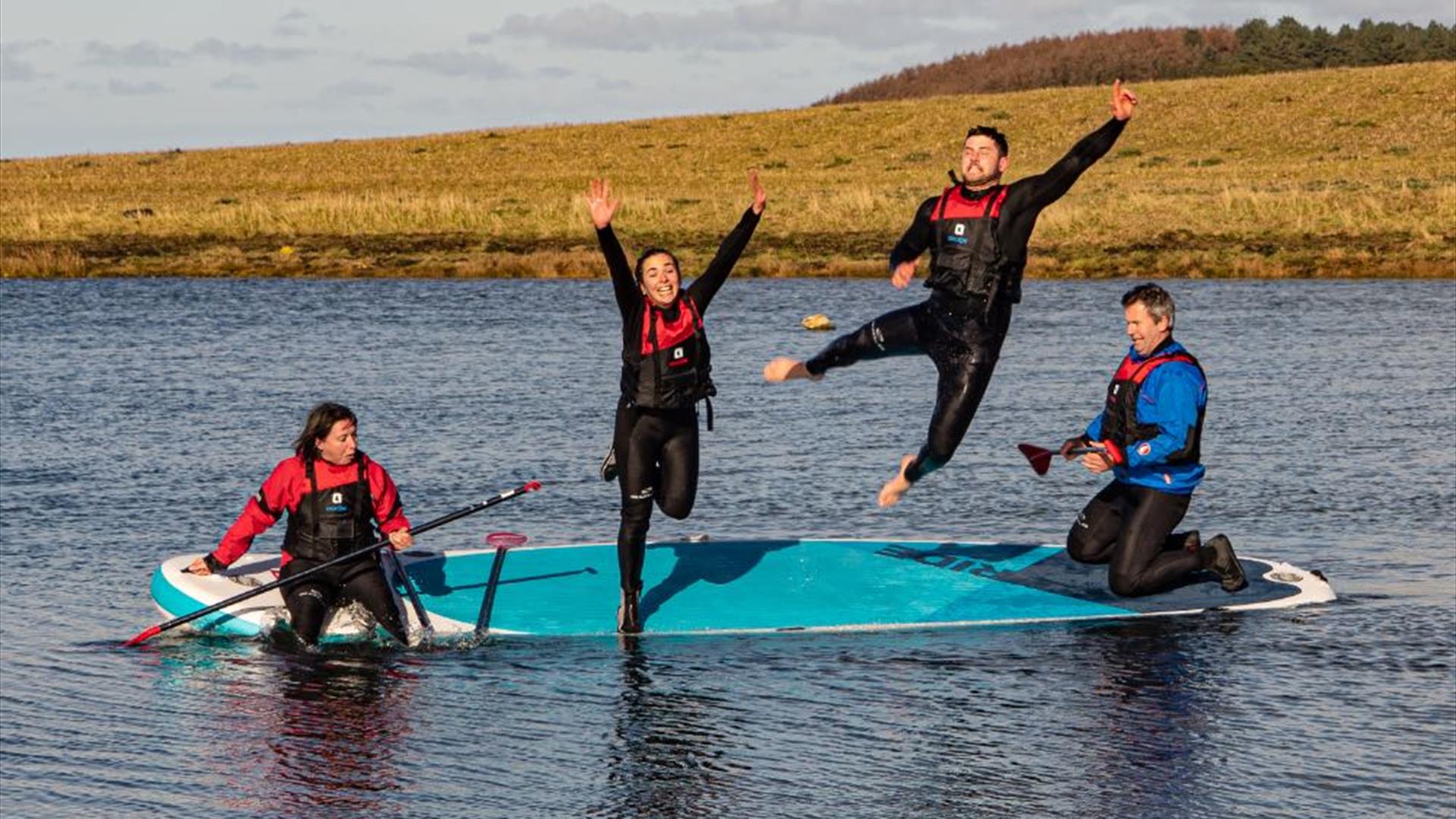 Four people jumping off a paddleboard into water