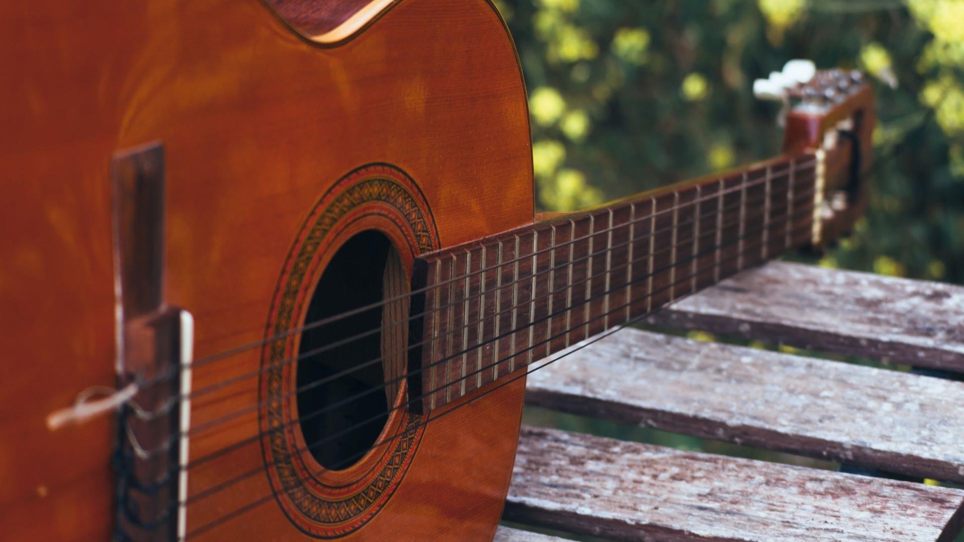 A close up of a guitar resting on a wooden table outdoors.