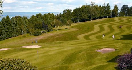 Golfers on the green with woodland and coast in background