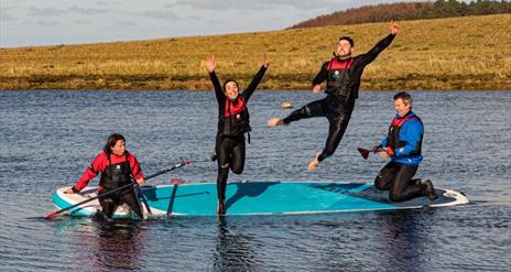 Four people jumping off a paddleboard into water