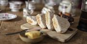 Wooden table laid with soda farls on bread board with butter, china tea set in background.